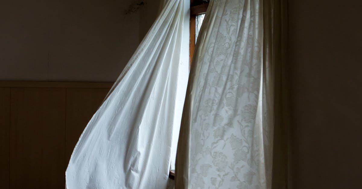 An empty room with open windows and flowing curtains creating an eerie atmosphere.