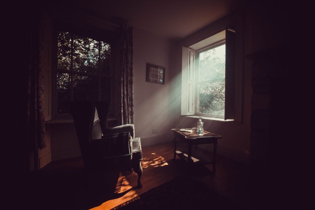 Bright sunlight shining through opened window of spacious rural house with classic styled armchair and wooden floor